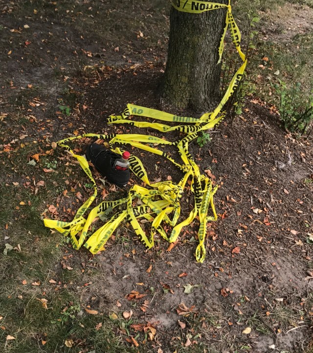 Black shoe with an empty liquor bottle wrapped in caution tape